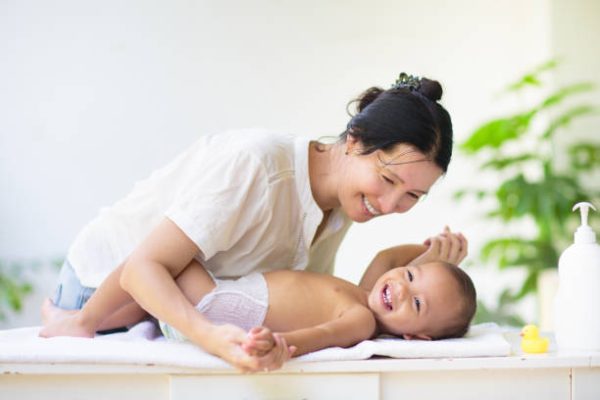 Mother changing diaper on newborn baby. Mom and laughing baby boy after bath or shower. Skin care for young kids. Asian woman changing nappy. Bathing and washing infant kid.