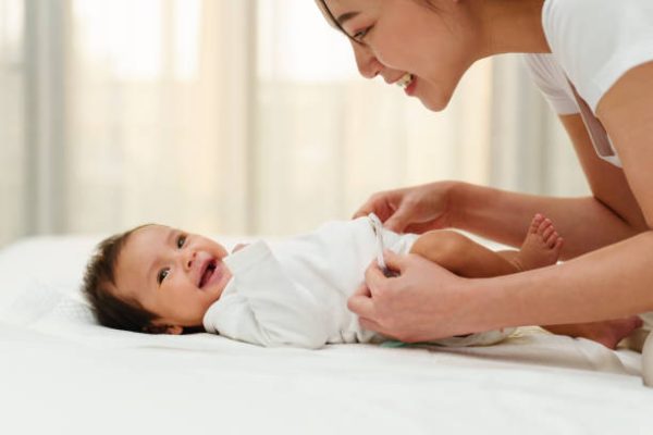 mother changing diaper of newborn baby while lying on a bed