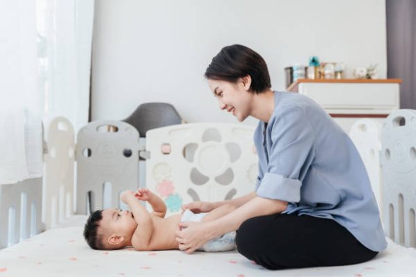 Asian baby shirtless lying on bed is changing diaper by his mother. Baby healthcare hygiene concept.